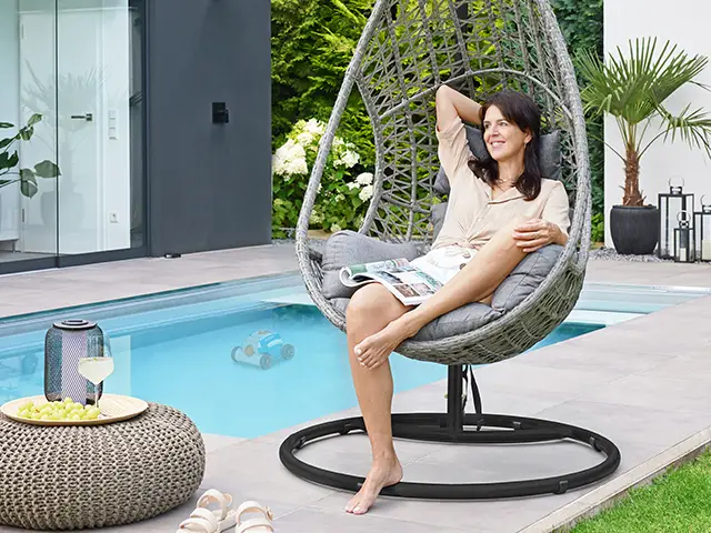 Eine Frau entspannt sich lesend in einem Hängesessel am Pool auf einer Terrasse.