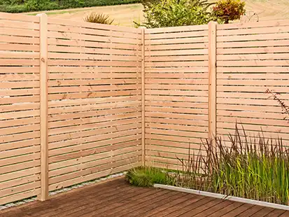 Ein Holzzaun steht in einer Ecke eines Gartens neben einem Holzdeck und Pflanzen.