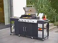 Ein Grillwagen bereitet Gemüse und steht auf einer Terrasse neben einem Gebäude mit Garten.
