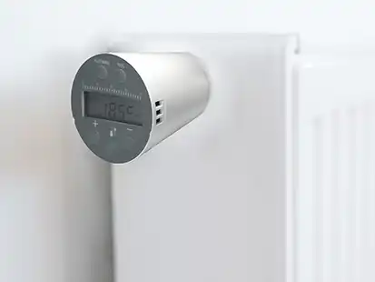 Ein Heizungsregler, der 18,5 °C anzeigt, ist an einem weißen Heizkörper befestigt.