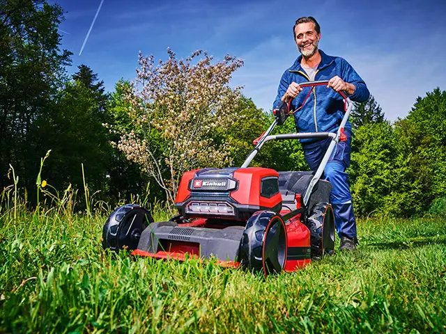 Ein Mann mäht mit einem roten Rasenmäher von Einhell die grüne Wiese.