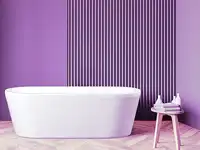 Eine weiße Badewanne steht vor einer lila gestreiften Wand auf einem Holzfußboden.
