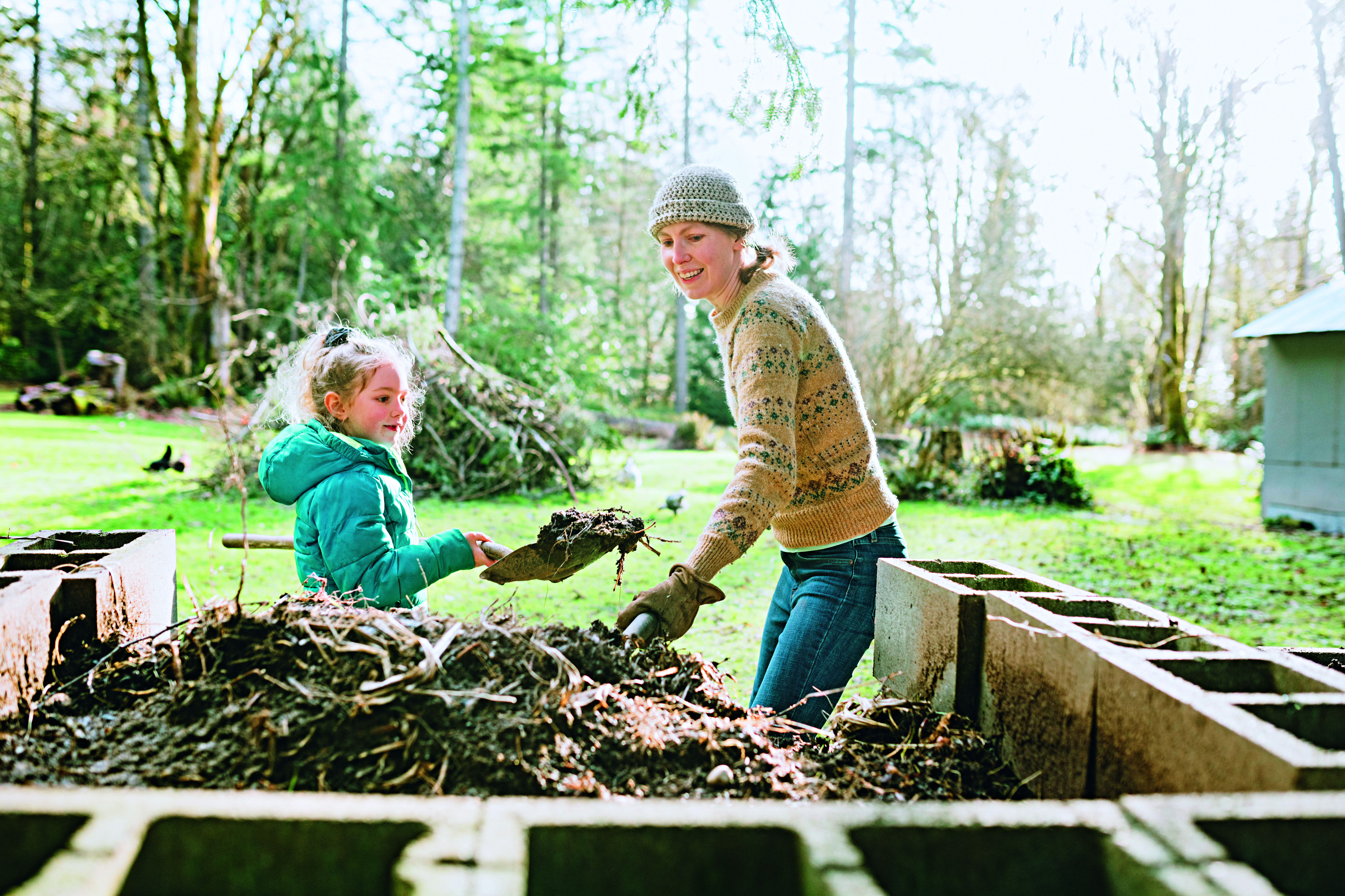 Eine Frau und ein Kind schaufeln Erde aus einem Komposter.