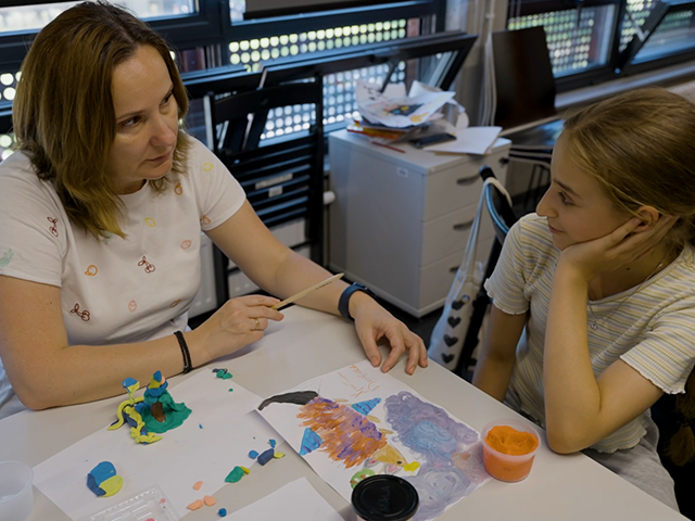 Eine Frau und ein Mädchen malen gemeinsam an einem Tisch in einem Klassenraum.