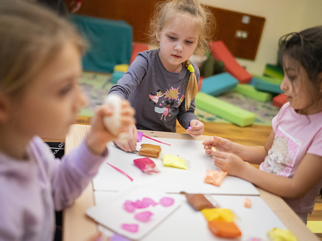 Drei Kinder basteln mit Knete an einem Tisch in einem bunt eingerichteten Raum.