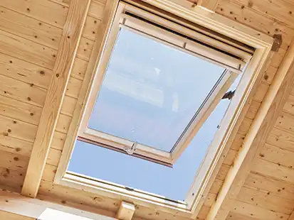 Ein geöffnetes Dachfenster lässt Tageslicht in einen Raum mit Holzwänden einfallen.