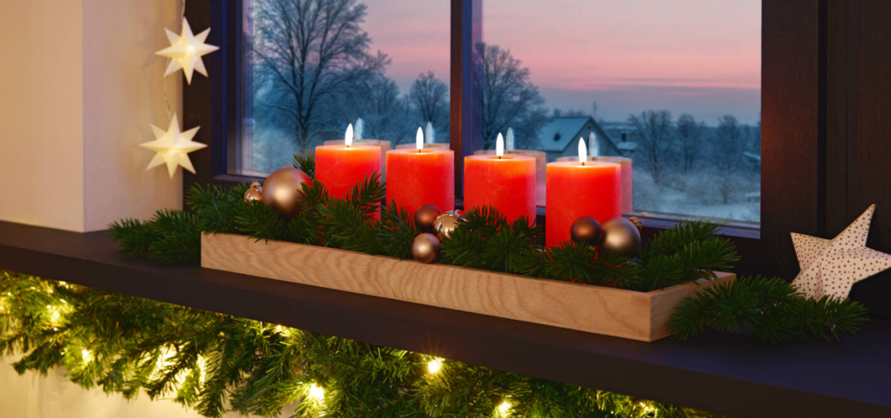 Adventskranz mit roten Kerzen auf einer geschmückten Fensterbank